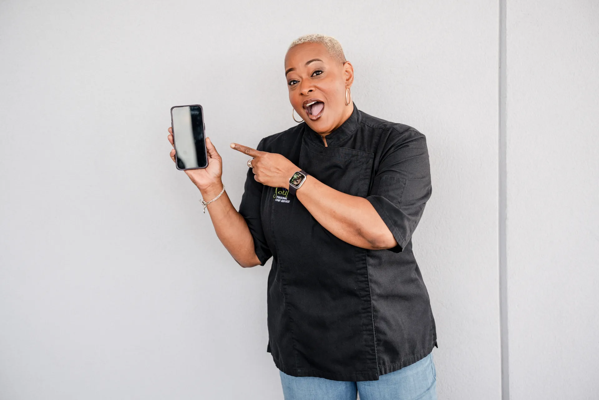 Chef Lisa Brooks in her chef coat pointing at her phone