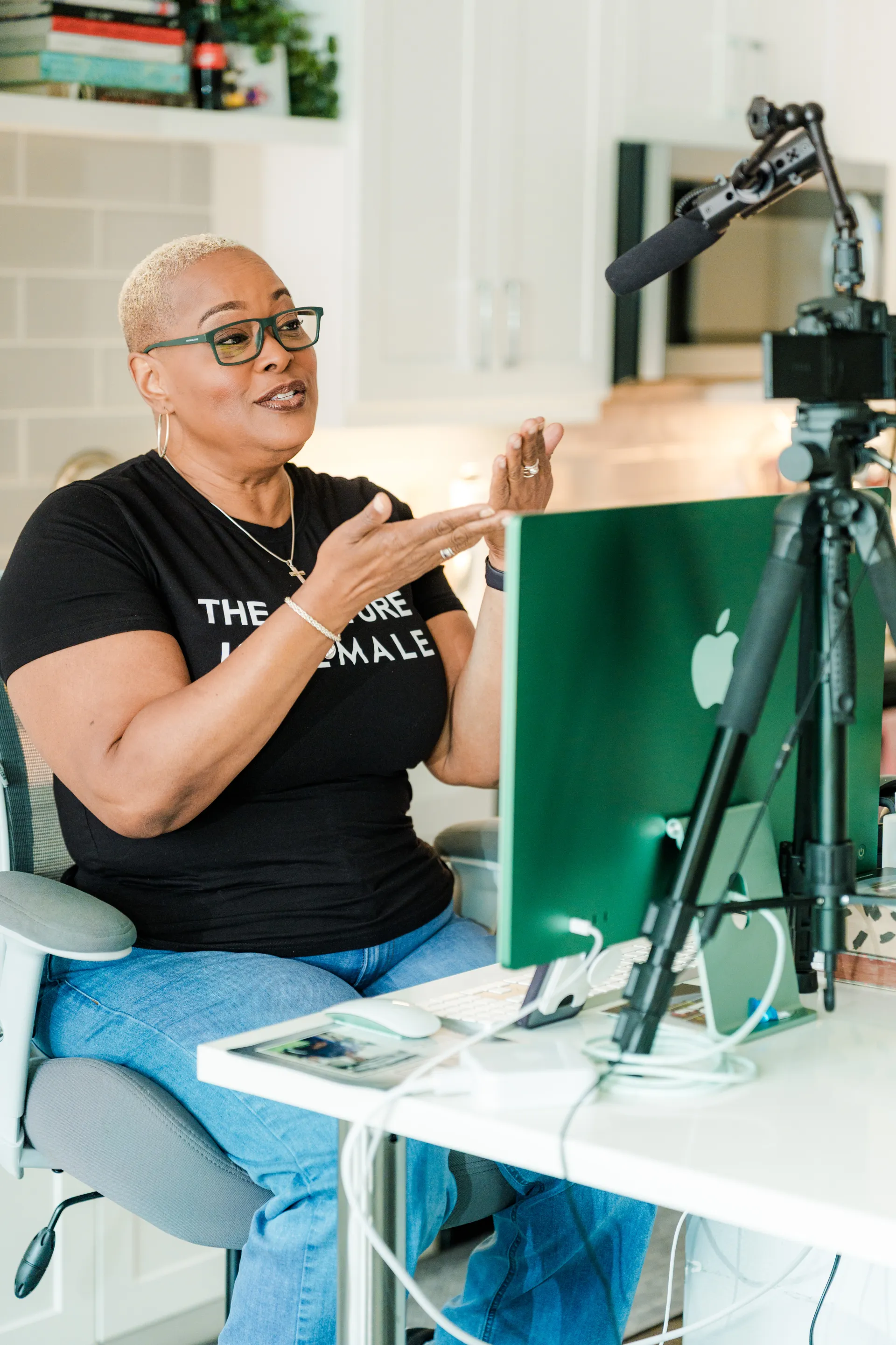 Chef Lisa Brooks at her desk with camera and tripod recording setup, gesturing while speaking